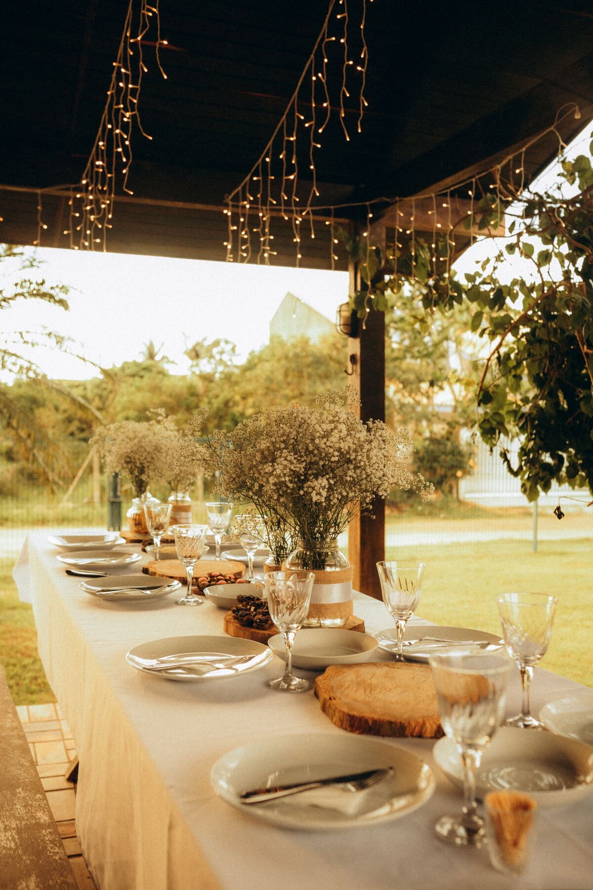 A long outdoor table under string lights, set for an evening meal