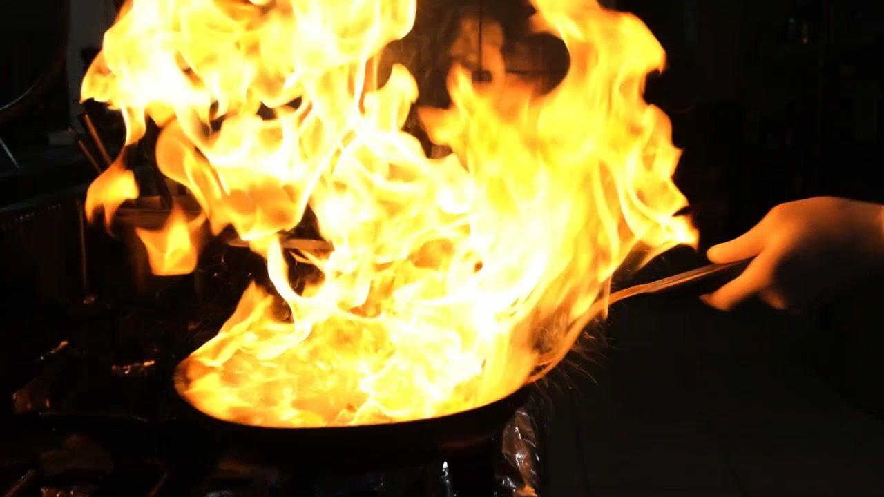 Flames rolling up around a pan in a dark kitchen