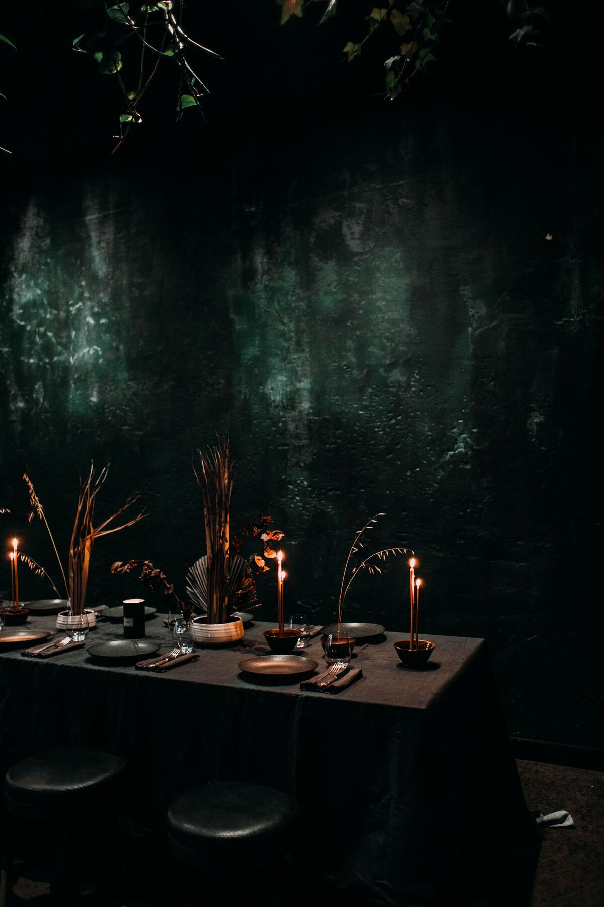 A long dark table set with candles and tall dried stems