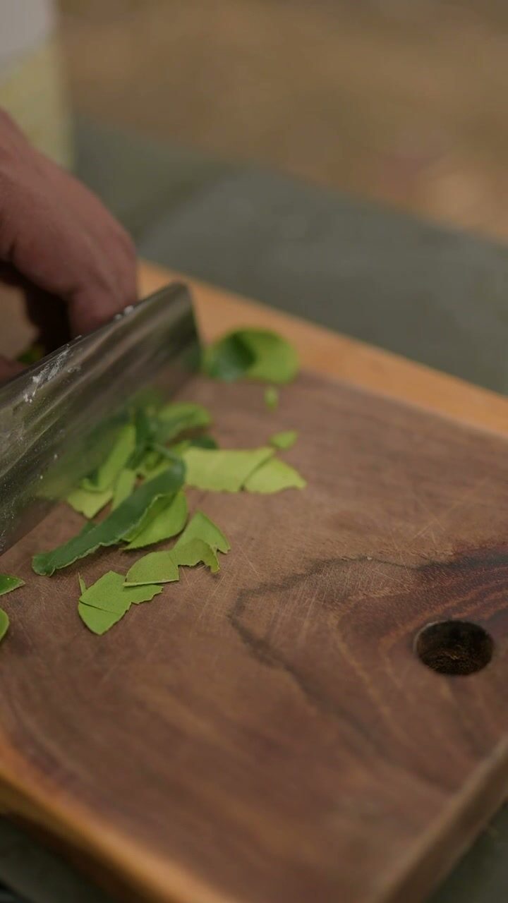 A knife working through fresh herbs on a wooden board